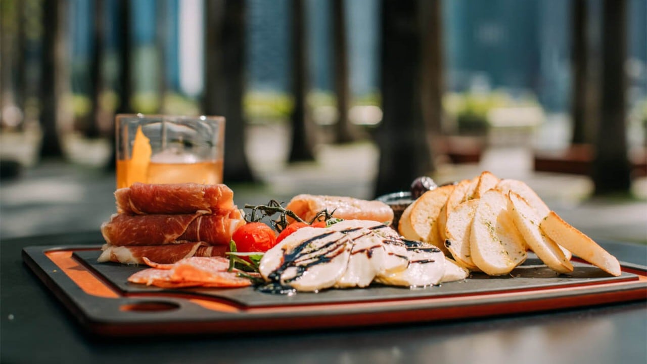 A glass of cocktail with cheese and ham platter for after-work drinks facing a waterfront bar